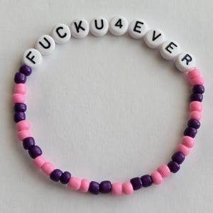 May include: A beaded bracelet with the text "FUCKU4EVER" spelled out in white letter beads. The bracelet features alternating sections of pink and dark purple beads, creating a two-tone design.