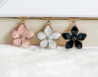 May include: Three gold flower-shaped bookmark charms. The charms are pink, white, and black.