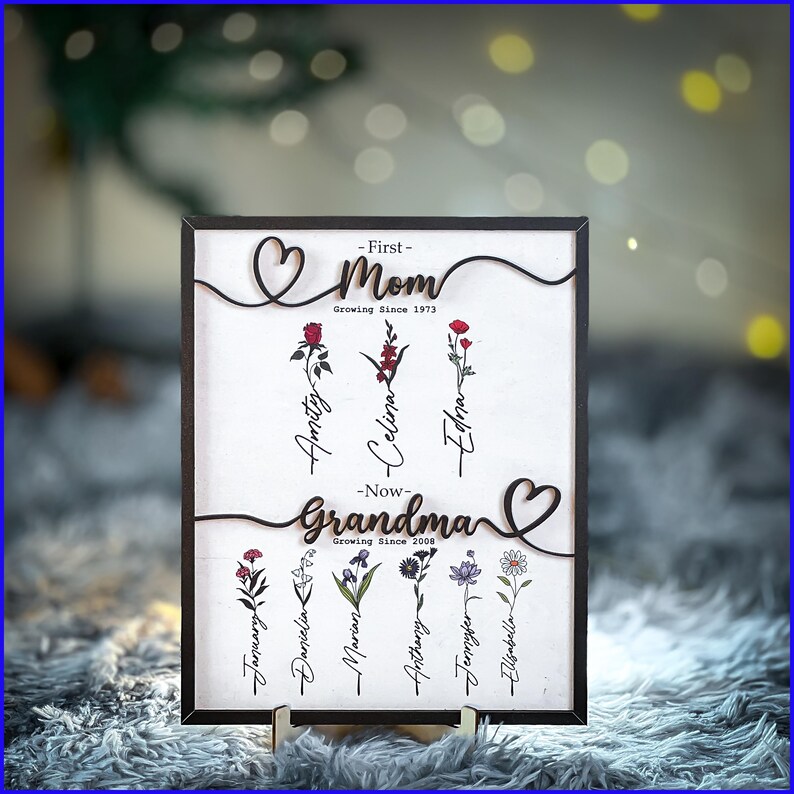 May include: A wooden plaque with a heart design and the words "First - Mom Growing Since 1973" and "Now - Grandma Growing Since 2008". The plaque features a floral design with names written on each stem.