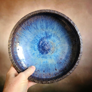 May include: A blue and brown ceramic bowl with a speckled glaze. The bowl has a deep, round shape and a wide rim.