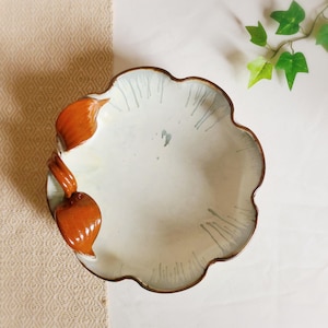 May include: A white ceramic serving bowl with a scalloped edge and two brown handles. The bowl has a light blue glaze with white streaks.