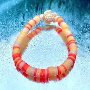 May include: A colorful beaded bracelet with a white turtle charm. The bracelet is made of orange, yellow, and white beads.