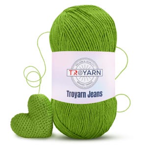 以下が含まれることがあります： 「Troyarn Jeans」と「信頼性の高い品質ブランド糸」と書かれたラベルが付いた緑色の糸の玉。手前に小さな緑色の編み物でできたハートがある。