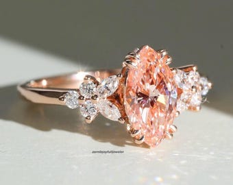 May include: A rose gold ring featuring a large marquise-cut peach-colored center stone flanked by smaller round and marquise-cut clear stones on each side. The band is smooth and polished. The text zarnibjoyfulijeweler is visible at the base.