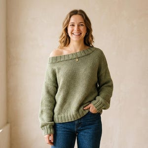 Könnte beinhalten: Ein salbeigrüner Strickpullover mit weitem, schulterfreiem Ausschnitt, langen Ärmeln mit gerippten Bündchen und einem gerippten Saum. Der Pullover wird mit einer dunkelblauen Jeans kombiniert. Das Kleidungsstück hat eine strukturierte Strickoptik.