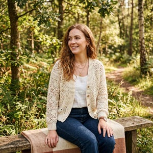 Könnte beinhalten: Eine cremefarbene, langärmelige Strickjacke mit Knopfleiste, die ein kompliziertes, durchbrochenes Häkelmuster auf der Vorderseite und den Ärmeln aufweist, kombiniert mit einem schlichten weißen Oberteil und einer dunkelblauen Jeans.