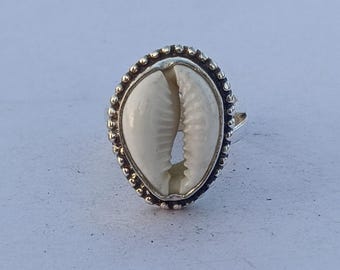 Könnte beinhalten: Ein silberner Ring mit einer weißen Kaurischnecke, die in eine Perlenfassung gefasst ist.