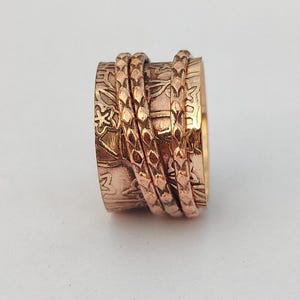 Può includere: Un anello rotante in rame con un design testurizzato. L'anello è composto da più bande che ruotano liberamente.