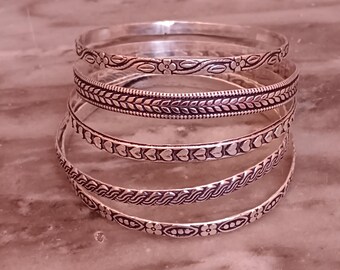 May include: Set of five silver bangles with different embossed designs. The bangles are stacked on top of each other, showing off the intricate details of each design.