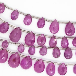 Op de afbeelding: Een streng roze edelsteen kralen, elke kraal is gefacetteerd en heeft de vorm van een traan. De kralen zijn geregen op zilverdraad.