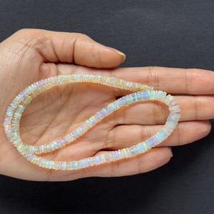 May include: A strand of white opal beads with iridescent rainbow flashes. The beads are small and round, and the strand is approximately 18 inches long.