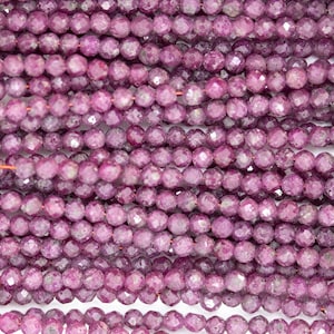 Może przedstawiać: Szereg fasetowanych fioletowych koralików z kamieni szlachetnych. Koraliki są okrągłe i mają lekko nieregularny kształt. Są nawleczone na drut.