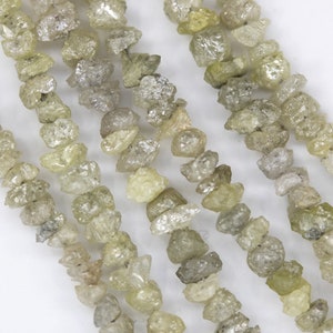 Puede incluir: Una hebra de cuentas de diamante en bruto, de color verde claro y gris. Las cuentas son de forma irregular y tienen un aspecto natural sin pulir.
