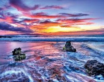 May include: A vibrant sunset over a calm ocean with pink, orange, and purple clouds. The water is a deep blue and there are rocks in the foreground.