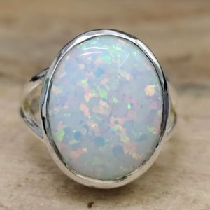 May include: A silver ring featuring a white opal gemstone. The opal has a milky white colour with iridescent flashes of pink and green.