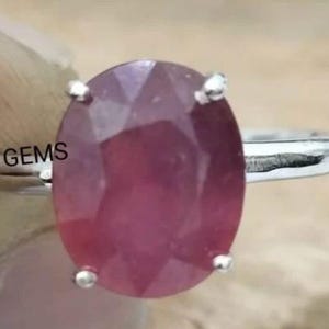 Pode incluir: Um anel de prata com uma grande gema oval rosa. O anel é adornado com pequenos detalhes prateados em torno da gema.