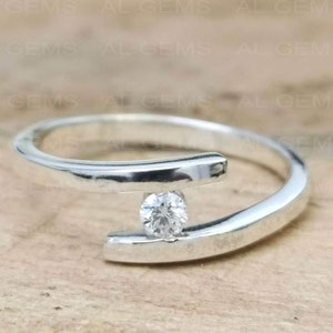 May include: A silver ring with a single, round, clear gemstone set in the center. The band is twisted and has a modern design.