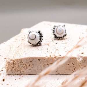 May include: A pair of silver earrings with white shell cabochons. The earrings have a beaded border around the shell.
