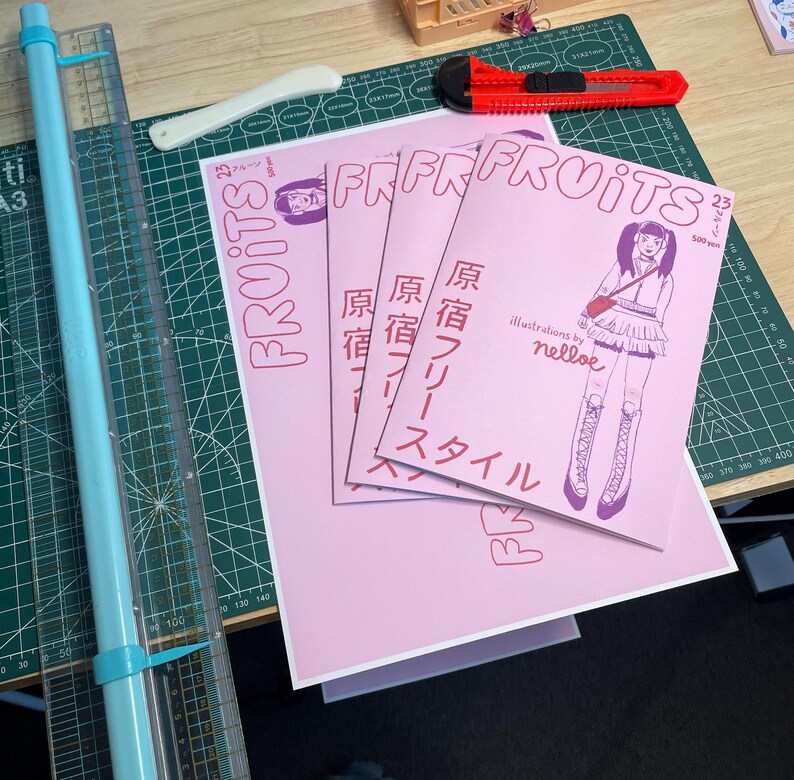 Pode incluir: Tr&ecirc;s revistas cor-de-rosa com o t&iacute;tulo "FRUITS" impresso em vermelho. As revistas est&atilde;o empilhadas umas sobre as outras. A revista superior tem o texto "Illustrations by nelloe" e "原宿フリースタイル" impresso em preto. A revista inferior tem o texto "FRUITS" impresso em vermelho.