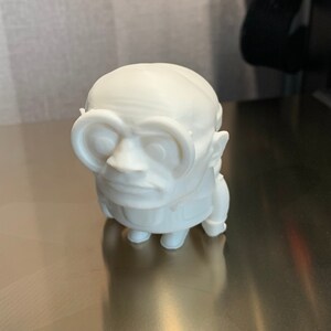 May include: White 3D printed figurine of a character wearing glasses. The character has a round head and a large nose.