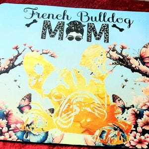 Könnte beinhalten: Ein hellblaues Mousepad mit einem French Bulldog-Design und dem Text "French Bulldog Mom". Das Design umfasst Schmetterlinge, Blumen und eine gelb-orangefarbene French Bulldog-Silhouette.