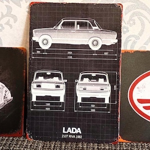 Può includere: Tre insegne metalliche vintage. Una mostra un diagramma esploso di un veicolo GAZ 69. La seconda insegna presenta un progetto di un'auto LADA. La terza insegna mostra il logo JAWA in rosso e bianco.