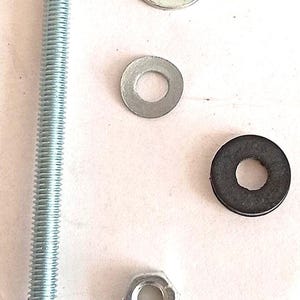 Könnte beinhalten: Eine Ansammlung von Metall-Hardware-Komponenten, darunter eine lange Gewindeschraube, flache Unterlegscheiben, eine Sechskantmutter und eine schwarze Gummiunterlegscheibe. Die Metallteile sind silberfarben.