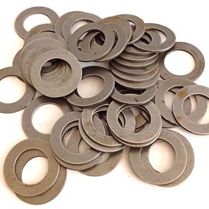 Könnte beinhalten: Ein Haufen zahlreicher, kreisförmiger Metallscheiben mit einem zentralen Loch. Die Unterlegscheiben sind von einem matten, silbergrauen Farbton und scheinen aus Stahl zu sein. Die Kanten weisen Gebrauchsspuren auf.