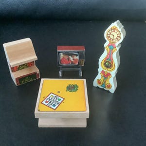 Könnte beinhalten: Ein Set aus Holzminiaturen für ein Puppenhaus, bestehend aus einem Kamin, einem Fernseher, einem Couchtisch mit einem Spielbrett und einer hohen Uhr mit gelbem, rotem und blauem Design.