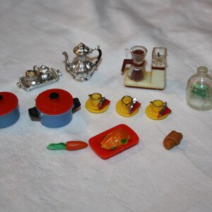 Könnte beinhalten: Eine Sammlung von Miniatur-Spielzeugküchenartikeln, darunter blaue Töpfe mit roten Deckeln, eine silberne Teekanne, eine Kaffeemaschine und gelbe Teetassen mit Untertassen. Enthält auch ein kleines Tablett, eine Flasche und Lebensmittel.