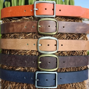 May include: Five leather belts with different colored buckles and straps. The belts are stacked on top of each other, with the top belt being orange, followed by brown, tan, dark brown, and navy blue.