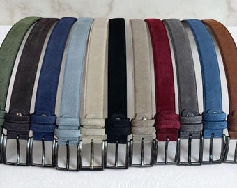 May include: A selection of suede belts in a range of colours: green, brown, navy, light blue, beige, black, burgundy, grey, and brown. Each belt features a silver-coloured rectangular buckle. The belts are displayed in a row against a white backdrop.