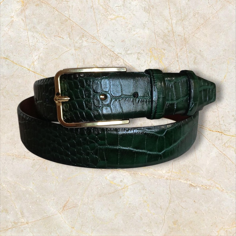 May include: A dark green belt with a textured, crocodile-like pattern. The belt features a gold-colored rectangular buckle and a matching belt loop. The leather belt is designed for waist sizes up to 40 inches.