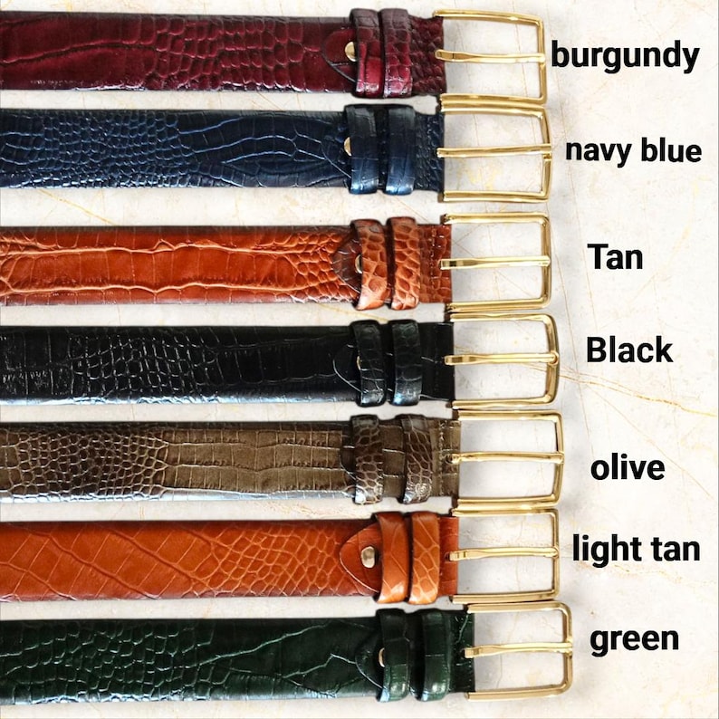 May include: A collection of seven leather belts in various colors, including burgundy, navy blue, tan, black, olive, light tan, and green. Each belt features a gold-colored buckle and a textured, crocodile-like pattern.