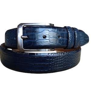 Op de afbeelding: Een marineblauwe riem met een textuurpatroon dat op krokodillenleer lijkt. De gesp is rechthoekig en zilverkleurig. De leren riem is opgerold, wat het ontwerp en de textuur laat zien.