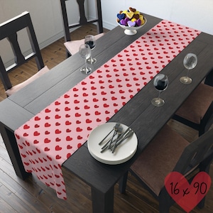 May include: A pink and red table runner with a heart pattern. The runner is 16 inches by 90 inches.