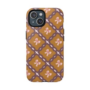 May include: A smartphone case featuring a repeating pattern of light pink bows centered within a grid of dark brown wavy lines on a mustard yellow background. The case has a circular cutout for the camera lens and a circular MagSafe ring visible.