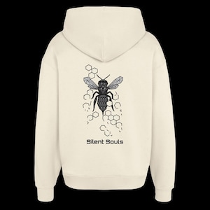 Könnte beinhalten: Ein cremefarbener Kapuzenpullover mit einer schwarzen, geometrischen Bienenillustration auf der Rückseite. Das Design zeigt eine Reihe von hexagonalen Wabenmustern um die Biene herum, mit dem Text Silent Souls in Schwarz unter der Grafik.