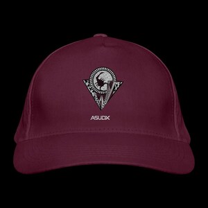 Könnte beinhalten: Eine kastanienbraune Baseballkappe mit einer mittigen Grafik, die ein kreisförmiges Emblem mit einer Skorpionsilhouette in einem Dreieck zeigt, verziert mit komplexen schwarz-weißen Mustern. Der Text ASUDX ist in Weiß unter dem Emblem gedruckt.