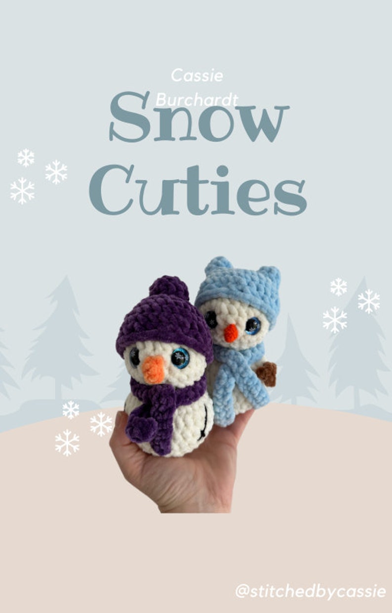 May include: Two small crocheted snowmen figures with plush white bodies and orange noses. One snowman wears a dark purple hat and scarf, while the other wears a light blue hat and scarf. The text Cassie Burchardt Snow Cuties is visible.