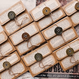 Puede incluir: Una colección de sobres de papel de estilo vintage, sellados con botones decorativos en forma de moneda y cuerda. Los sobres presentan papel envejecido con texto impreso, creando una estética rústica y antigua. Las palabras "DUCK SOUP" son visibles.