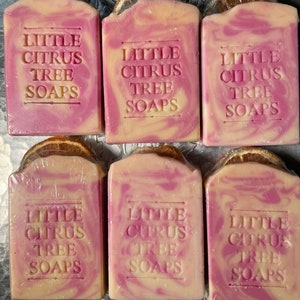Könnte beinhalten: Sechs handgemachte Seifen mit einem Wirbel aus Rosa und Gelb. Die Seife ist mit "Little Citrus Tree Soaps" gekennzeichnet.