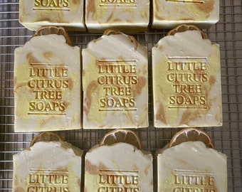 Könnte beinhalten: Neun handgemachte Seifen mit einem marmorierten Design in Weiß- und Gelbtönen. Jede Seife trägt den Aufdruck "Little Citrus Tree Soaps".
