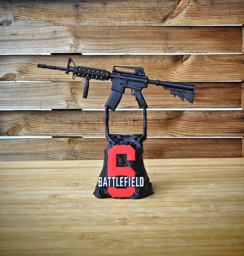 May include: A black rifle model is displayed above a black base with the number "6" in red and the word "BATTLEFIELD" below it. The background is a wooden wall.