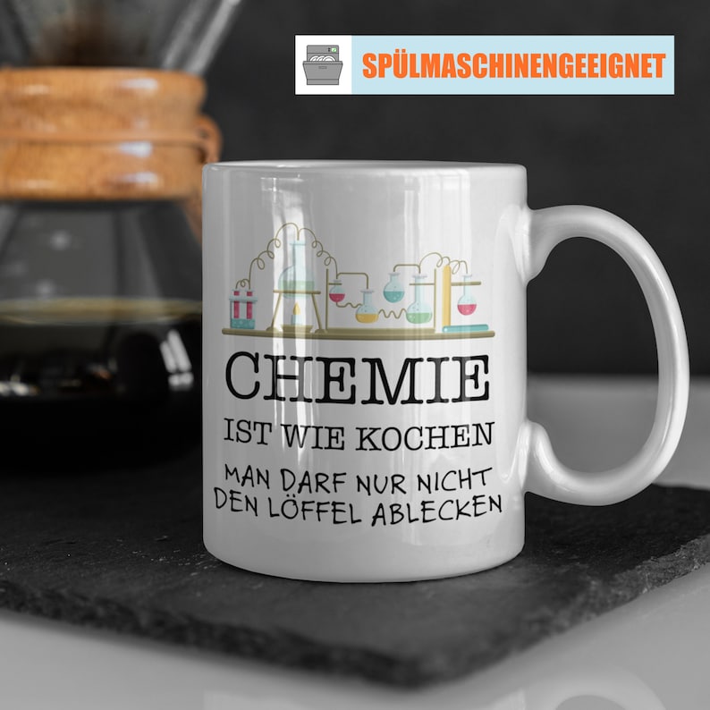 Puede incluir: Taza de cer&aacute;mica blanca con asa, con la palabra "CHEMIE" en letras negras grandes, junto con texto en alem&aacute;n y un gr&aacute;fico con tem&aacute;tica de laboratorio. La taza tambi&eacute;n tiene el texto "SP&Uuml;LMASCHINENGEEIGNET" en la parte superior.