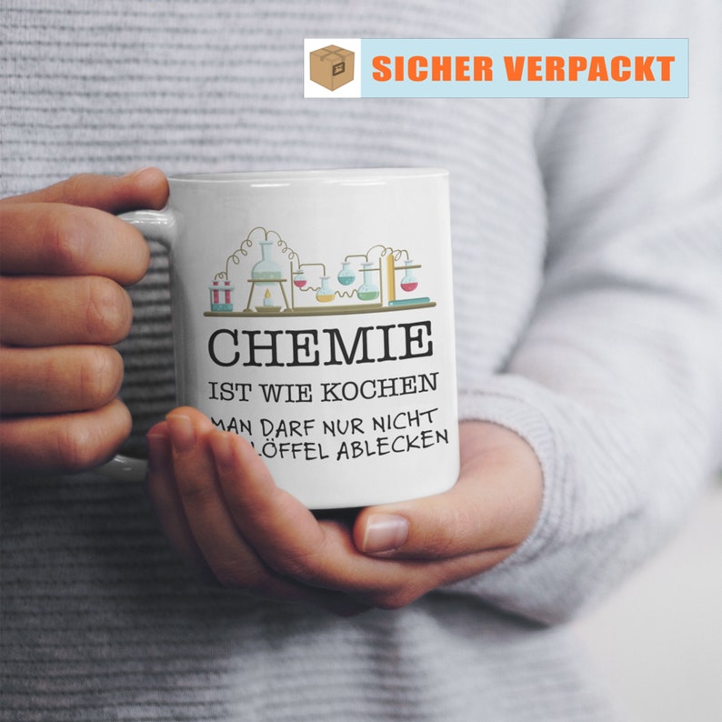 Puede incluir: Taza de cer&aacute;mica blanca con un dise&ntilde;o tem&aacute;tico de qu&iacute;mica, con vasos de precipitados y matraces. La taza tiene el texto "CHEMIE IST WIE KOCHEN MAN DARF NUR NICHT L&Ouml;FFEL ABLECKEN". La taza es sostenida por una persona.