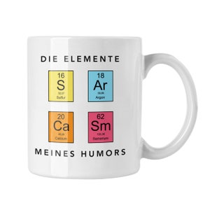 Könnte beinhalten: Weiße Keramiktasse mit dem Text "DIE ELEMENTE MEINES HUMORS" und Elementen des Periodensystems: Schwefel, Argon, Calcium und Samarium. Die Tasse hat einen gebogenen Henkel.