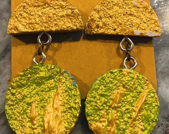 May include: A pair of gold and green earrings with a textured finish. The earrings are made of two pieces, a half-circle and a round disc. The half-circle is gold and the round disc is green with gold accents.