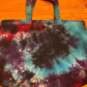 May include: A large, tie-dye tote bag with a black, blue, and red swirl pattern. The bag has two long, black straps.