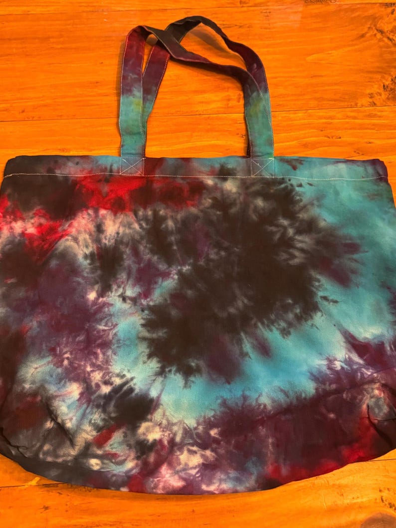 May include: A large, tie-dye tote bag with a black, blue, and red swirl pattern. The bag has two long, black straps.
